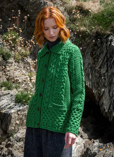 Red head model wearing emerald green jackie aran lumber cardigan at bottom of cliff face
